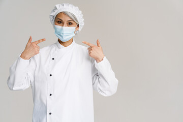 Asian mature woman in white chef uniform gesturing at her face mask