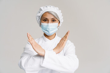 Asian mature woman in chef uniform and face mask gesturing stop sign