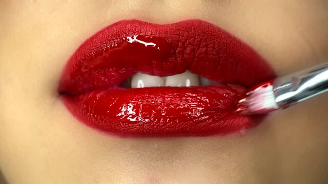 Close-up view of female mouth while applies a make-up. Creative makeup artist puts on a lipgloss on a model's lips. High quality 4k footage