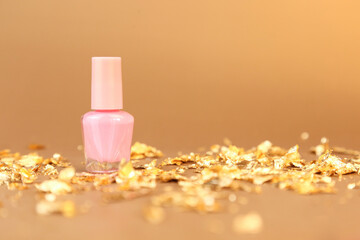 Nail polish small glass bottle and gold paper pieces on golden background. Unbranded mockup with copy space. Professional manicure concept.