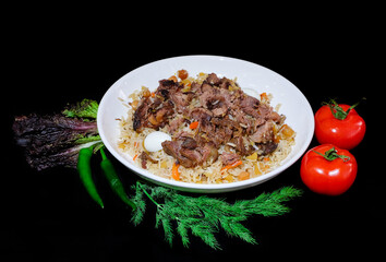 Asian plow dish with rice and meat, with greens, lettuce, hot pepper and tomatoes
in a white dish on a black background