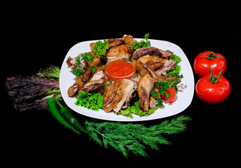 pieces of fried chicken with greens, lettuce, hot pepper and tomatoes
in a white dish on a black background