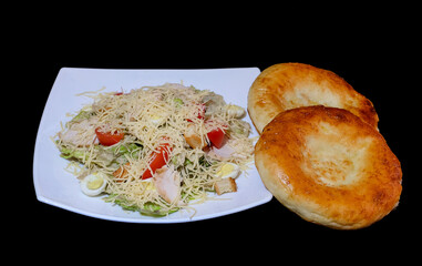 salad with chicken, vegetables, greens, tomatoes, cheese and two tortillas in a white dish on a black background