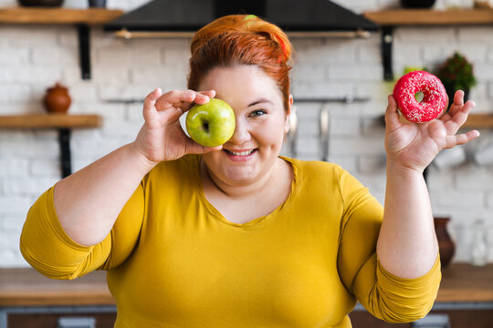 Plump Fat Obese Young Caucasian Woman Covering Her Eyes With Donut And Apple. Healthy Dieting And Eating Habits Concept. Losing Weight On Diet