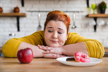Portrait of a confused young woman choosing between donut and red apple. The choice. Two options. The choice between eating. Delema, for a healthy lifestyle or not.