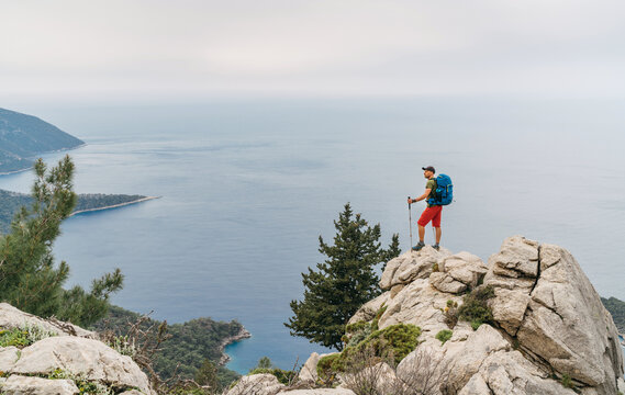 Young backpacker man with trekking poles enjoying the Mediterranean Sea on clifftop during Lycian Way trekking walk. Famous Likya Yolu Turkish route near Letoon. Active people vacations concept image