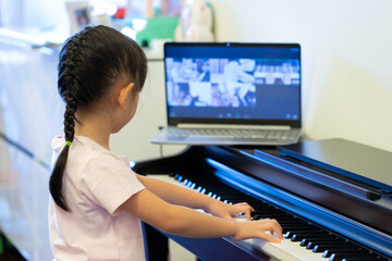 a little asian girl play piano while learning piano online class.