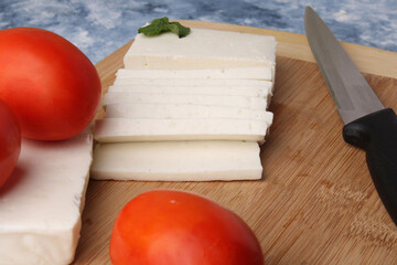 sliced fresh paneer or cottage cheese with tomatoes and knife on cutting board.