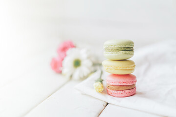 Obraz na płótnie Canvas Beautiful flowers and macarons standing on top of each other in different colors against a white background. Gift to a loved one