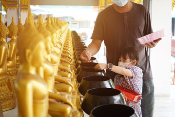 Asian little girl put mask and make merit at the temple. Buddhist make merit, Pay coins