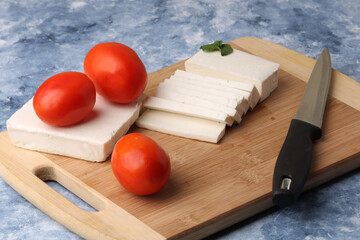 sliced fresh paneer or cottage cheese with tomatoes and knife on cutting board.