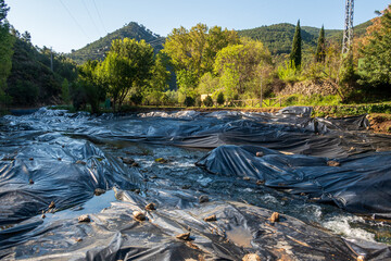 Black plastic awnings covering the side of a river to prevent the growth of invasive reeds (Arundo Donax).