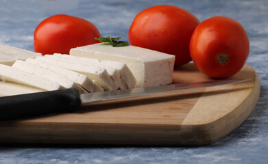 sliced fresh paneer or cottage cheese with tomatoes and knife on cutting board.