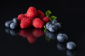 Mix of berries raspberry blueberries on a dark background with reflection isolated macro