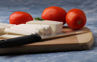 sliced fresh paneer or cottage cheese with tomatoes and knife on cutting board.