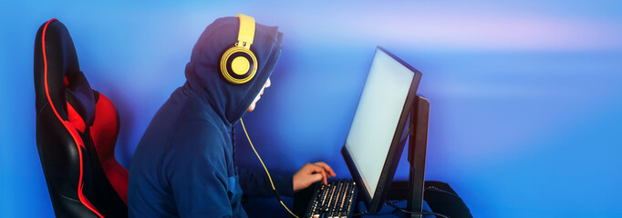 The gamer sits on a gaming chair and plays computer games. The player has yellow headphones on his...