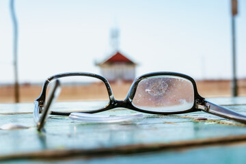 Fototapeta na wymiar Lost and broken prescription eye glasses sit on a picnic table with the Leuty Lifguard Station building in the background in Toronto’s Beaches neighbourhood.