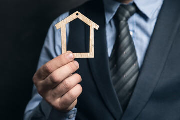 businessman holding a wooden house in his hand