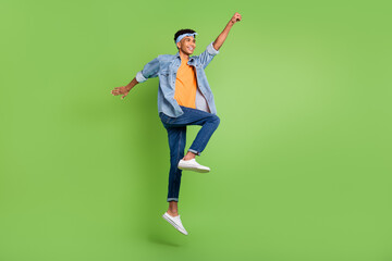 Profile photo of guy jump raise fist look empty space wear headband jeans shirt sneakers isolated...