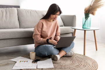 Focused woman working on laptop sitting on floor at home