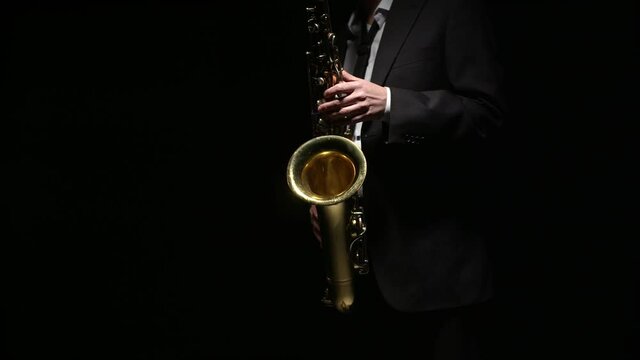 Man plays with hands on the saxophone keys. Musician in a suit plays the saxophone in darkness. Symphony orchestra.