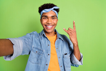 Photo of guy take selfie show fingers horns wear piercing headband jeans shirt isolated green color background