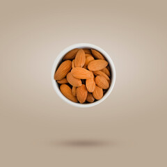 White ceramic bowl filled with almonds flies freely on a beige background. Food levitation concept. Monochrome image.