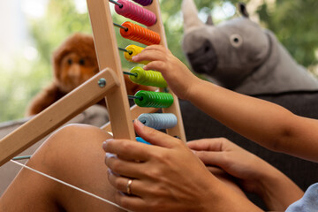 Close up capture of hands of mother and child playing with wooden colorful abacus with plush toys in frame