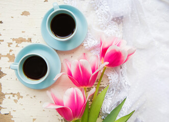 two cups of coffee and pink tulips on an old table