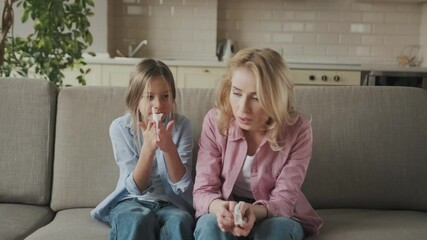 Sad caucasian mother and daughter with a cold are sitting at home on the sofa with napkins, sneezing, coughing, runny nose. Cold, flu, illness - Powered by Adobe