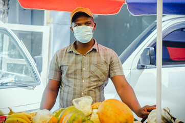 young dark-skinned man of Haitian nationality working selling fruits in the street with a bicycle and an umbrella and wearing a mask