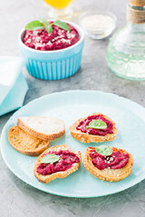 Homemade bruschetta with beetroot hummus on small baked baguette toast on a plate and a bowl of hummus on the table. Vertical view