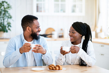 Fototapeta na wymiar Domestic Morning. Young Happy Black Couple Having Coffee And Croissants For Breakfast