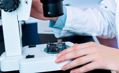 A young woman is testing an electronic module for the production of electric cars. Quality control...