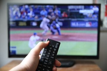 Hand holding the remote controller against the blurred TV screen/Baseball broadcast