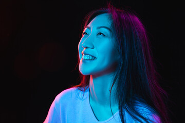 Asian young woman's portrait on dark studio background in neon. Concept of human emotions, facial...