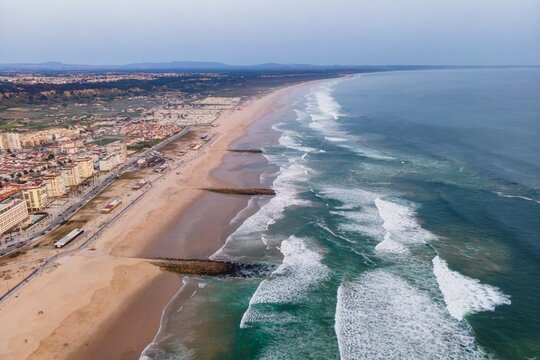 Aerial view of Costa da Caparica landscape at sunset, view of the majestic beach with rough Atlantic Ocean rolling on the shoreline, Setubal, Portugal.