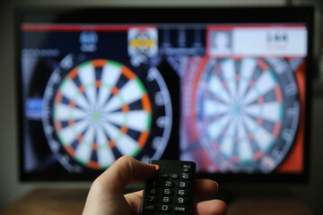 Hand holding the remote controller against the blurred TV screen/ Dart-throwing broadcast