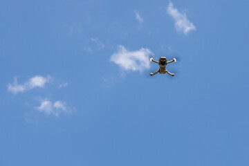 White unmanned aerial vehicle with four propellers and blades is on the blue sky background