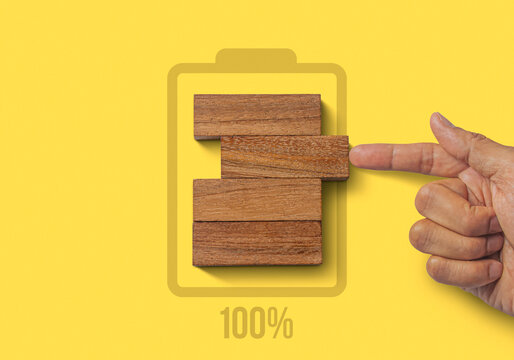 Fully charged, recharge, reboot, refresh or mindset concept. Hand putting wooden blocks with the battery charger and 100% icon on yellow background.