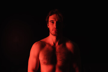 Fototapeta premium red lighting on sexy shirtless man looking at camera isolated on black.