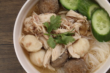 Clear white rice vermicelli beehoon noodle soup with chicken beef meat ball shredded cucumber in white bowl chopsticks spoon chili soya sauce parsley garnish