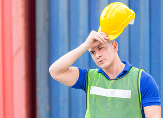 Factory worker taking off yellow safety helmet at the cargo container