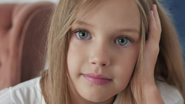 Close up portrait of cute little blonde caucasian girl with big eyes looking at camera. Portrait of adorable preschool american kid child sitting. Concept of children