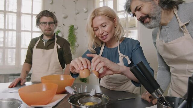 Slow-motion medium shot of attractive Caucasian woman with small group of people enjoying cooking at culinary school, practicing making poached egg, cracking egg into strainer