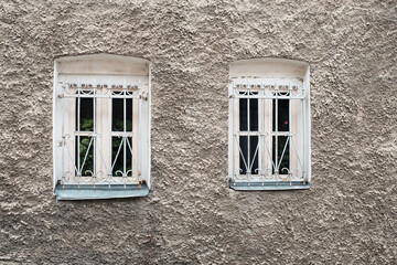 Two white windows behind the iron bars on the shabby wall of the building