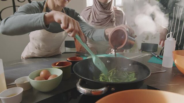 Slow-motion midsection shot of unrecognizable woman practicing cooking during culinary class adding some soy sauce to frying green beans