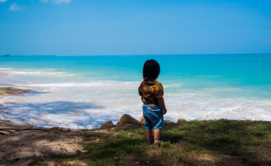 A boy stands looking at the sea at Laem Son Beach, Ban Nam Khem, Takua Pa District, Thailand