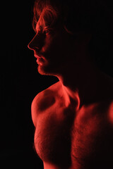 red lighting on sexy shirtless man looking away isolated on black.