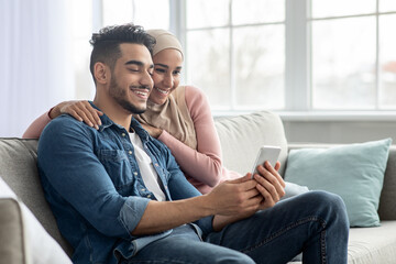 Happy middle-eastern couple using mobile phone at home - Powered by Adobe